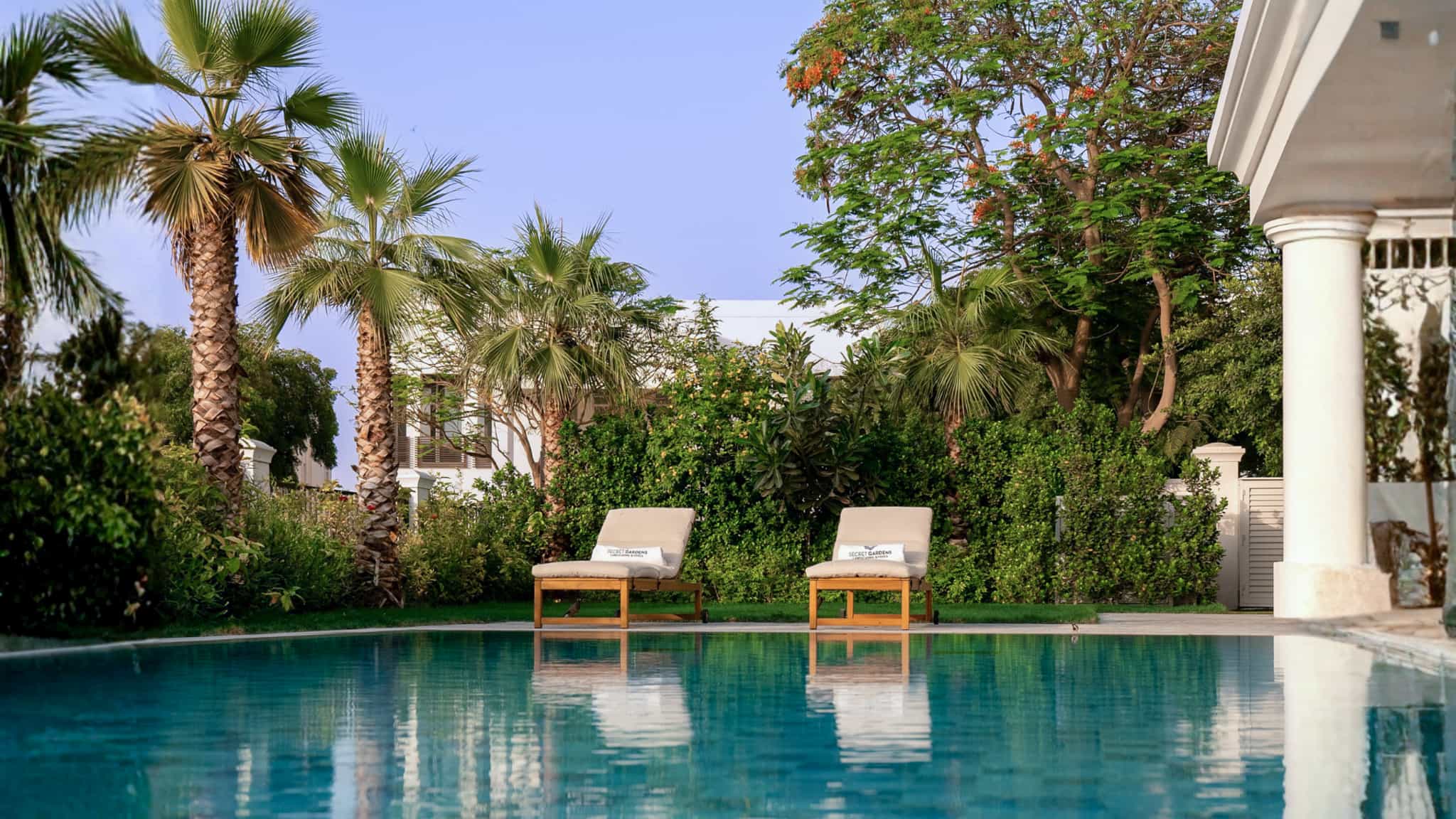 Poolside landscape design in an Emirates Hills villa garden with mature palms and shaded loungers, Dubai