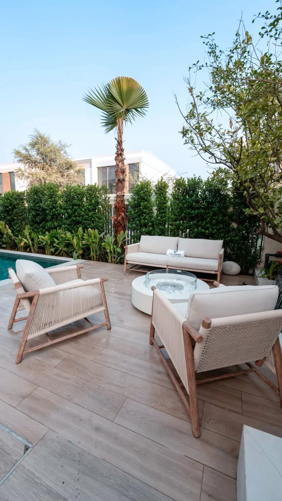 Poolside landscape design in Tilal Al Ghaf, Dubai with a circular glass fire pit table, lounge seating and palm planting
