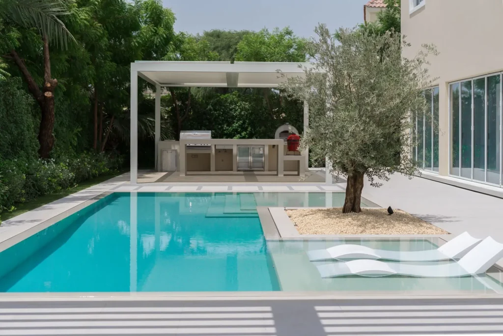 Villa pool with olive tree planter, sun shelf loungers and outdoor kitchen pergola